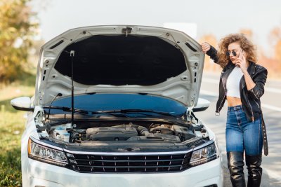 Young woman standing near broken car with popped hood
